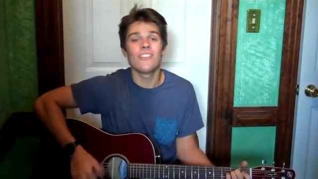 Cole in a blue t-shirt singing with his acoustic guitar