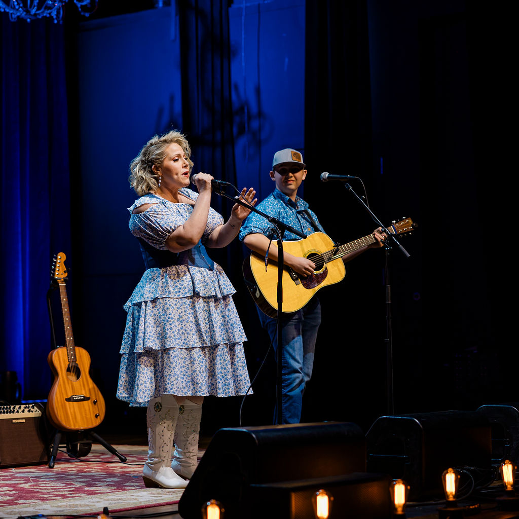 Vocalist in blue dress singing with guitarist behind her
