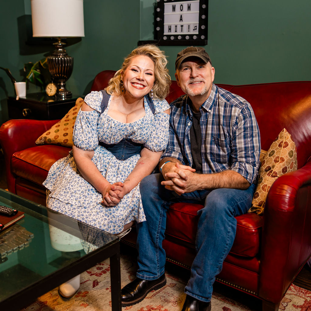 Two people posing on a red leather couch beneath a WOW A HIT sign